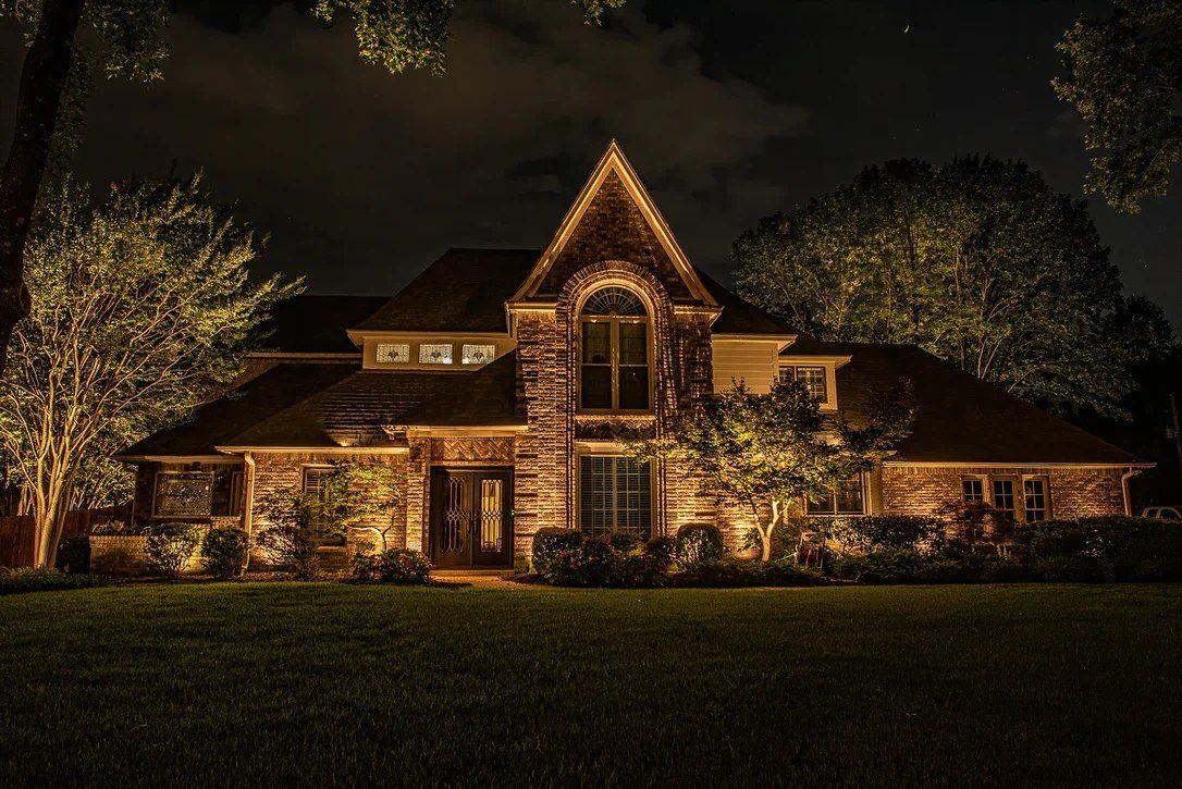 Large home with evening uplighting and turf